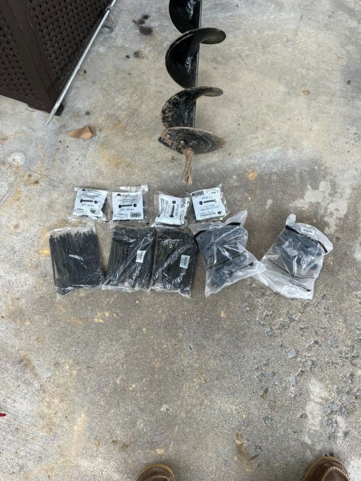 An auger drill and several packages of black cable ties and hardware on concrete.