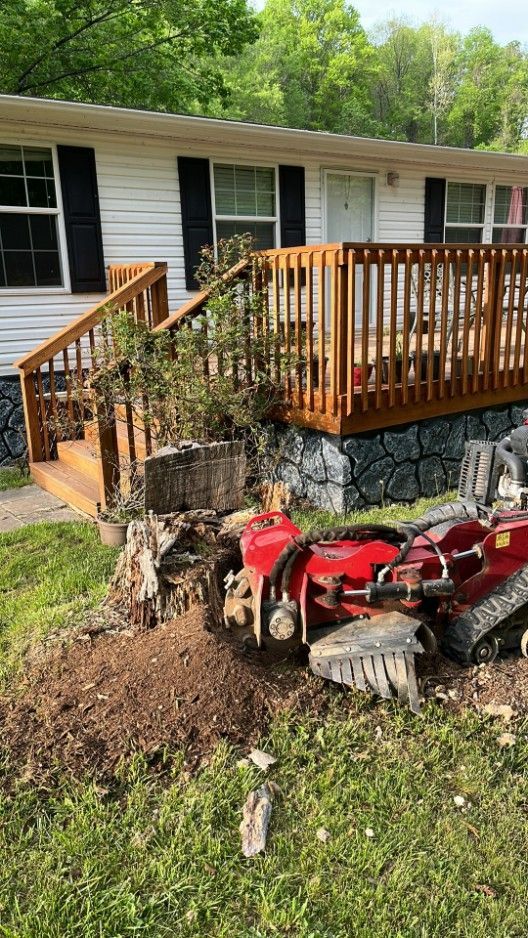 Stump grinder in front yard, grinding a tree stump near a house with a wooden deck.