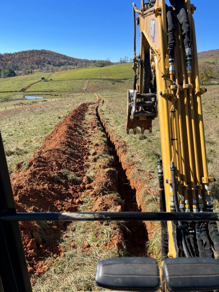 An excavator digging a trench in a grassy field on a sunny day.