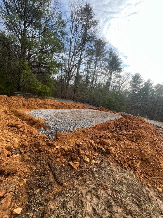 Newly excavated area with gravel base, surrounded by red soil, near trees.