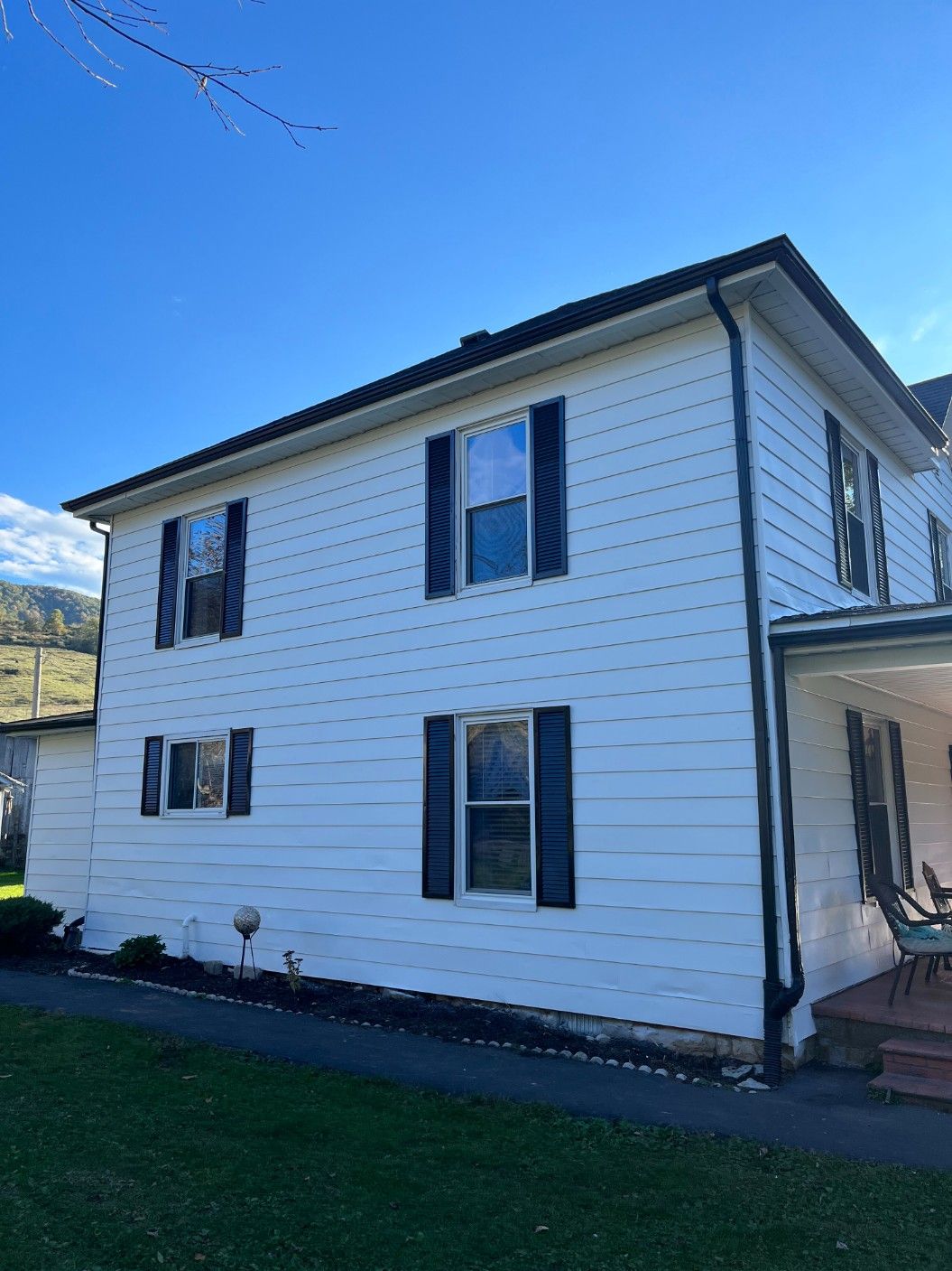 White two-story house with black shutters, roof, and trim under a blue sky.