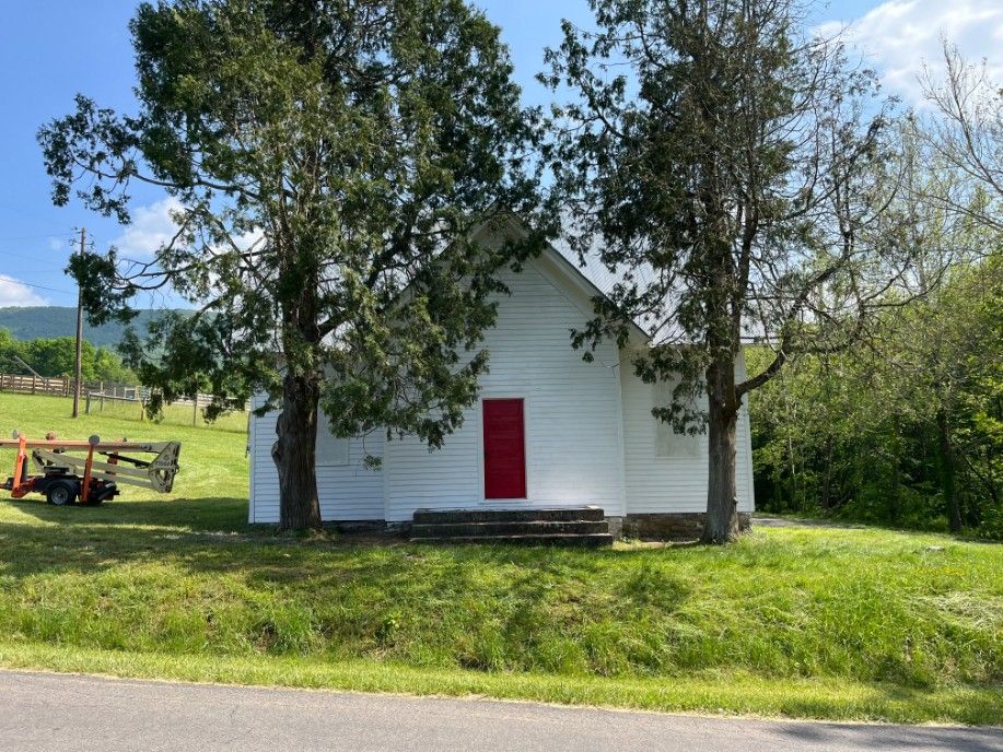 White building with red door, framed by trees, in a grassy field.