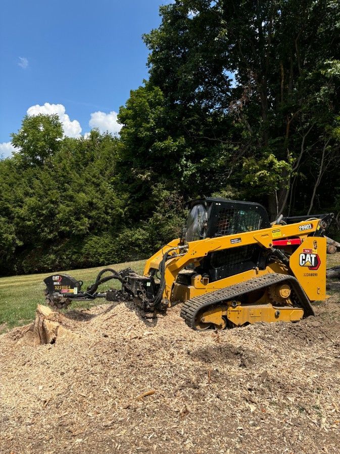 Yellow Caterpillar stump grinder removing a tree stump in a yard on a sunny day.