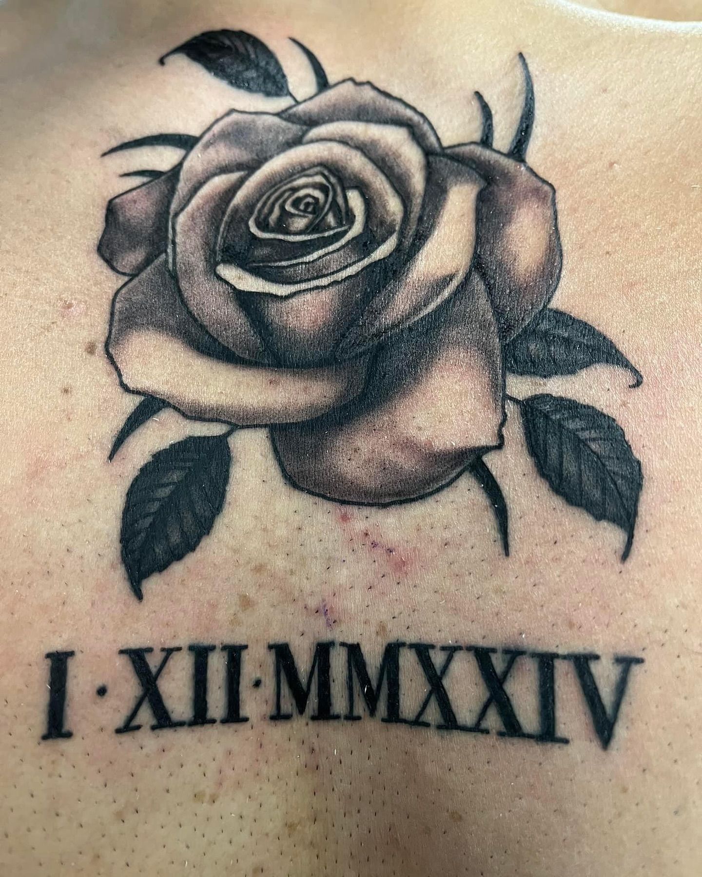 A black and white tattoo of a rose and roman numerals