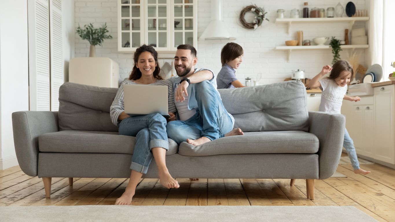 a family is sitting on a couch with a laptop .