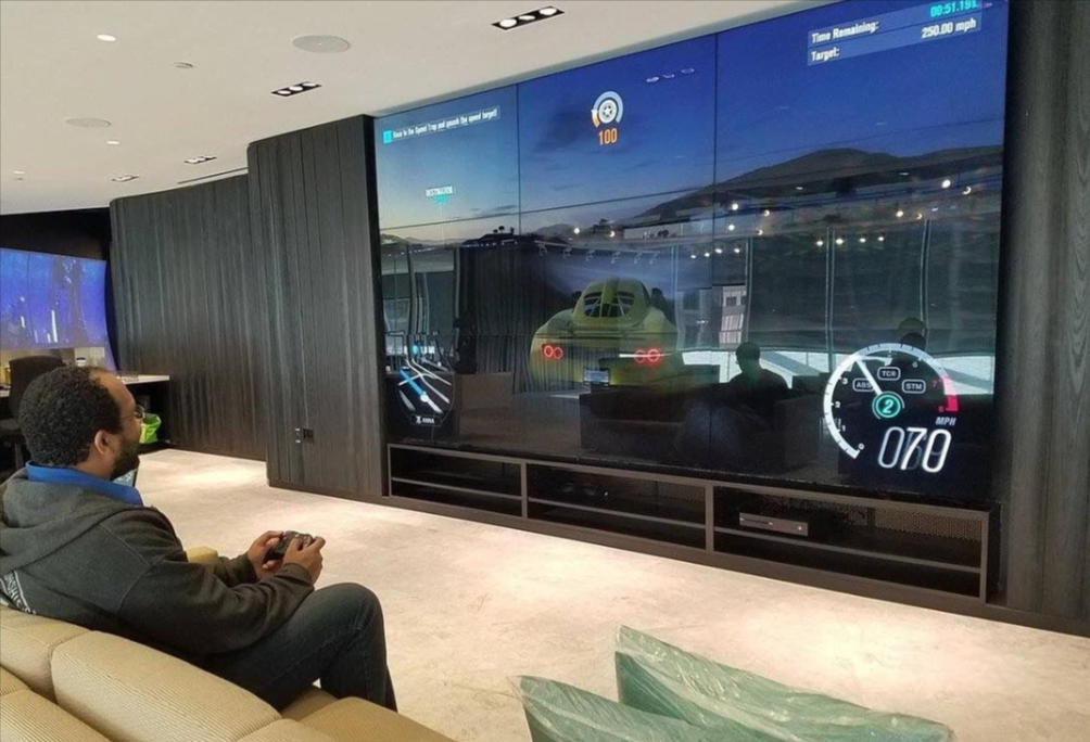Gaming on a media room Man playing a racing game on a massive wall-mounted screen. The screen displays a car racing scene, with a speedometer visible.