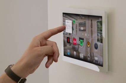 Wall mounted white smart home control4 touchscreen. Device is being used by a person's finger touching the screen.