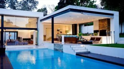 A modern white house with a large swimming pool in front of it next to a deck.