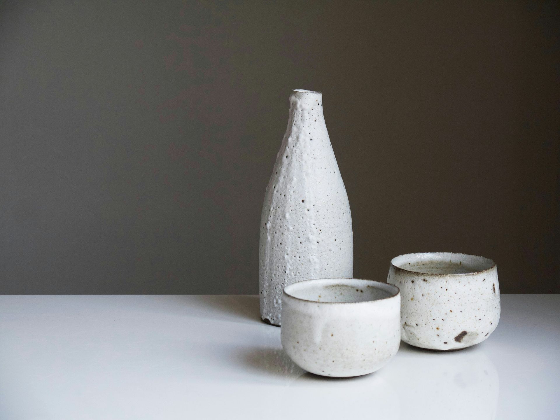 Minimalist ceramic bottle and two handmade cups with a speckled white finish on a clean surface
