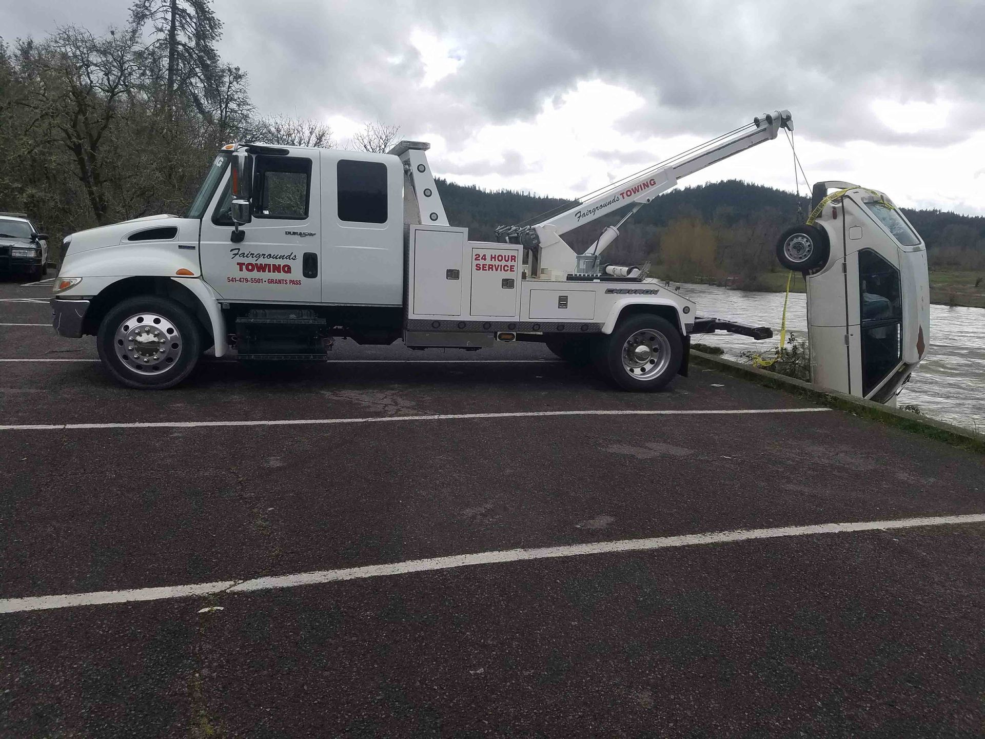 Tow truck towing an overturned white van on a road near a guardrail.