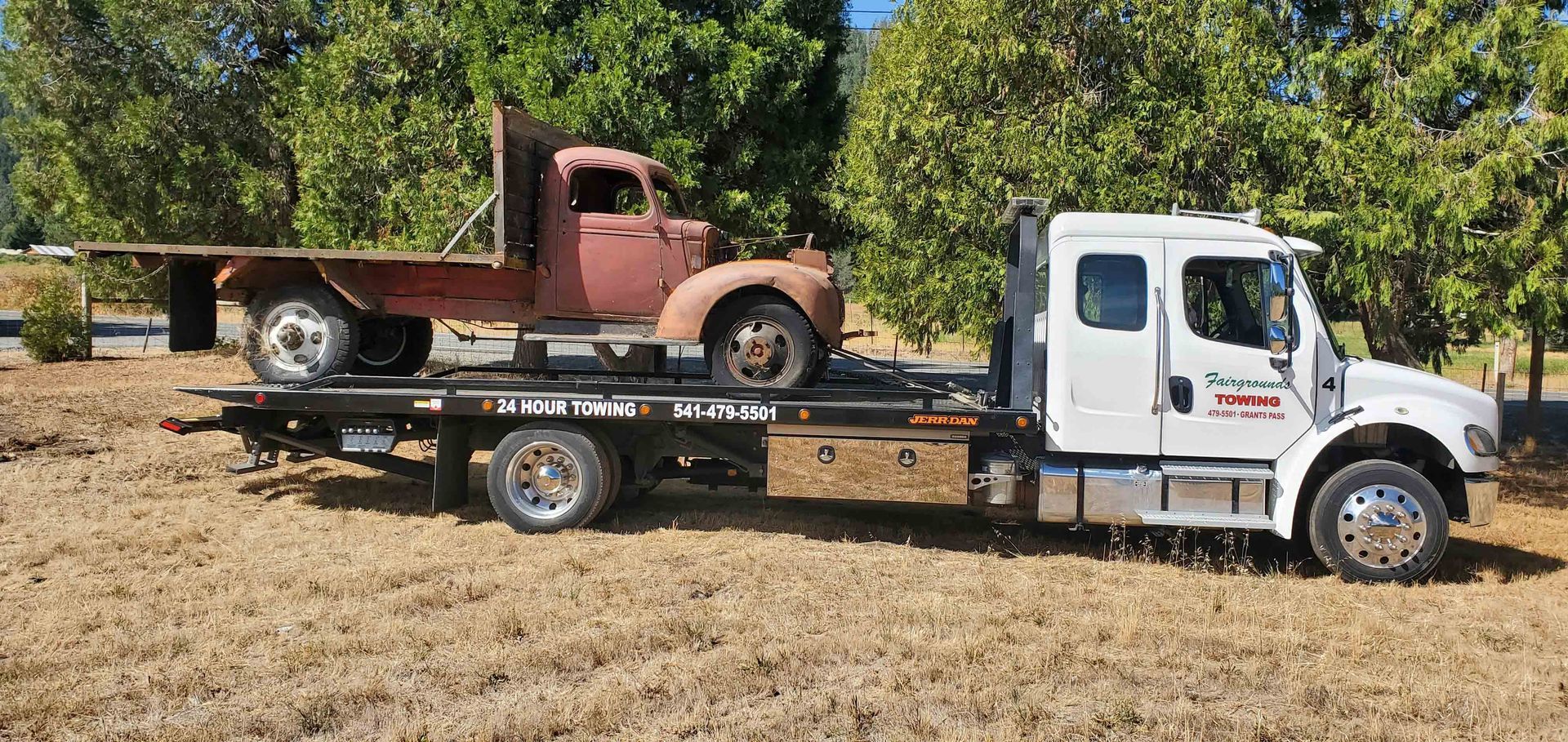 White flatbed truck carrying an old rusty pickup in a dry field