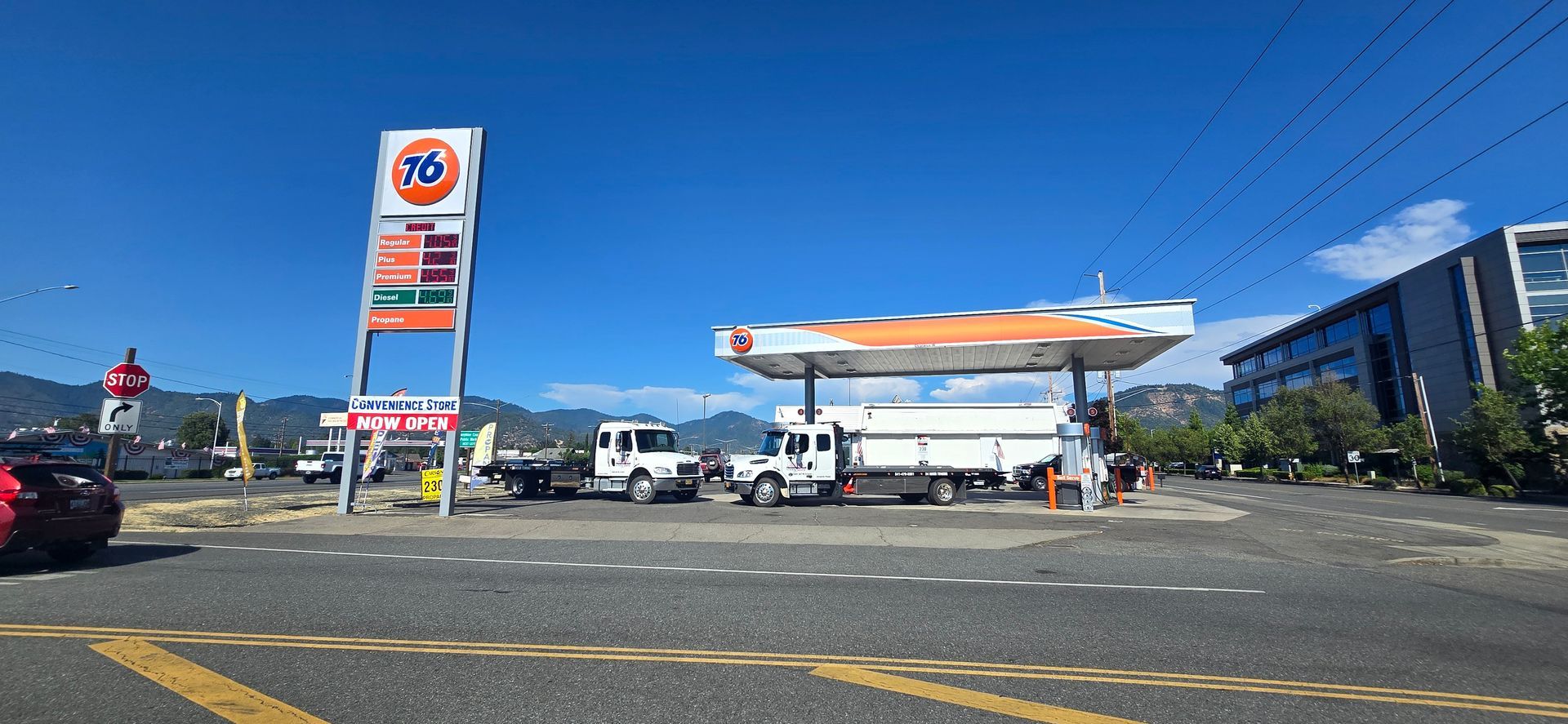 Gas station on a sunny day with parked trucks, a tall sign, and a blue building in the background