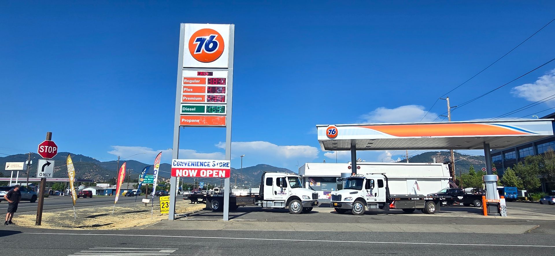 76 gas station with a tall sign, fuel pumps, trucks, and an orange canopy under a blue sky