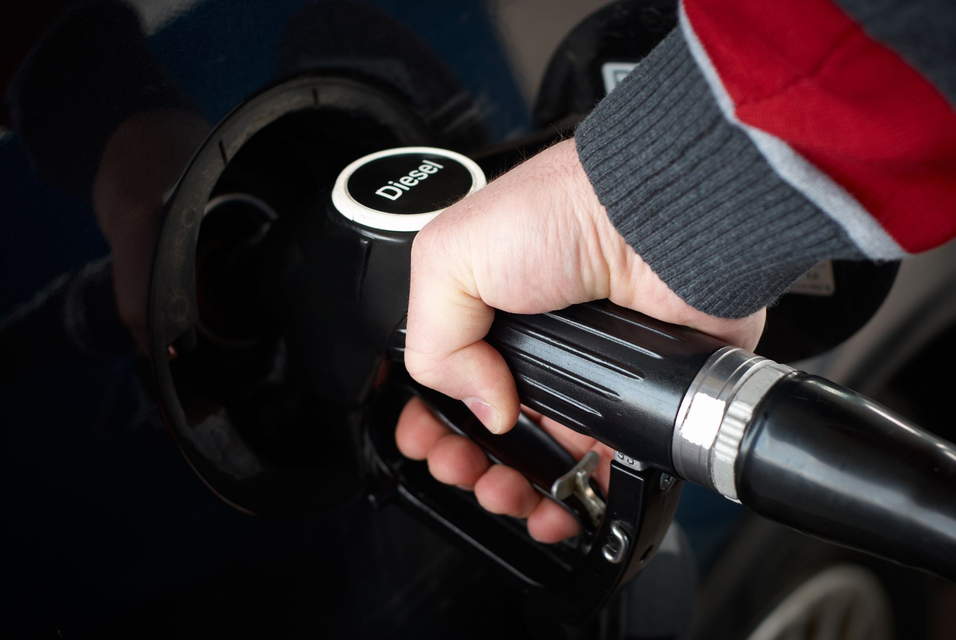Hand holding a diesel fuel nozzle while refueling a vehicle at a gas station. Hand refueling a car with a black fuel nozzle at a gas pump