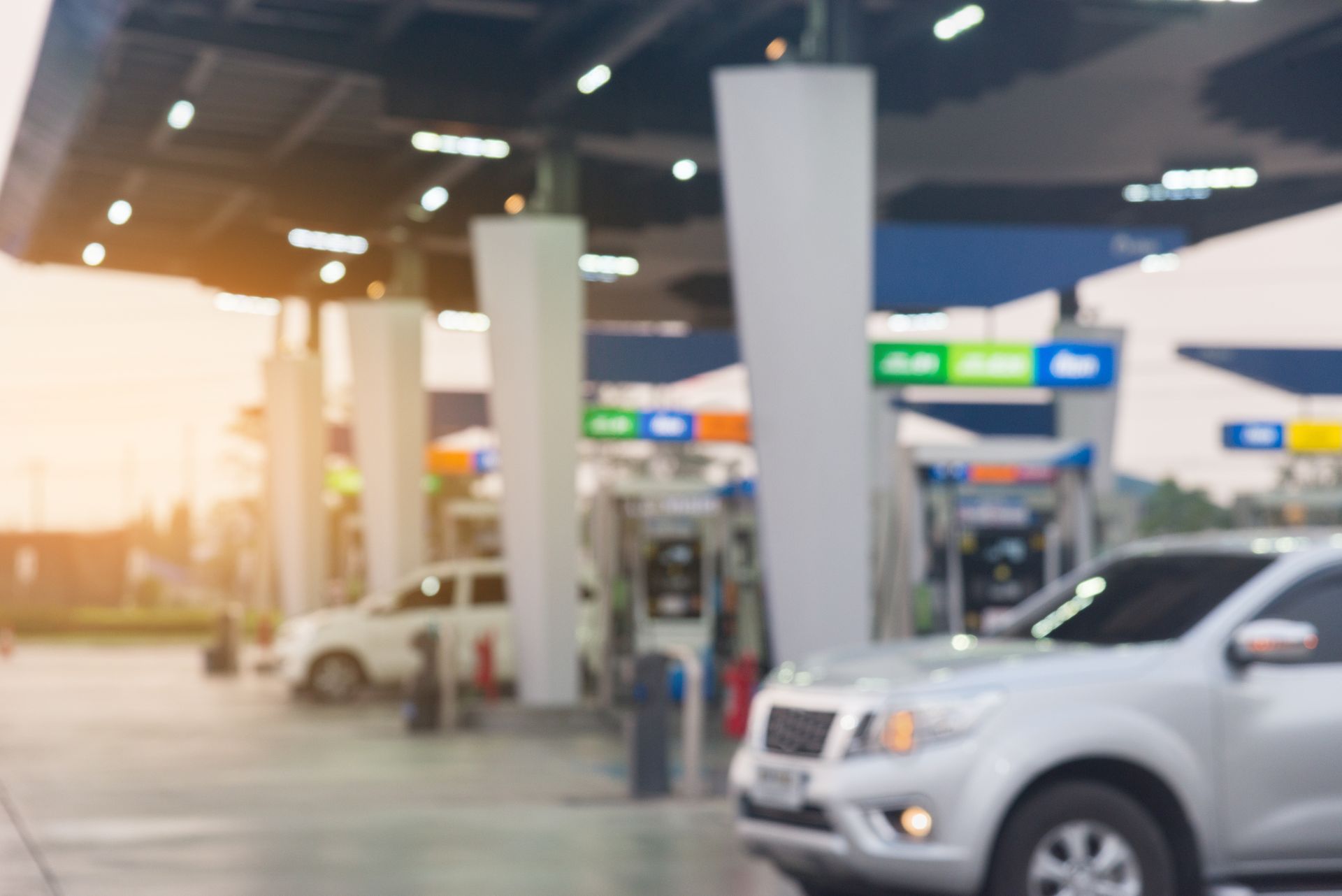 Gas station forecourt at dusk with parked cars and bright overhead lights