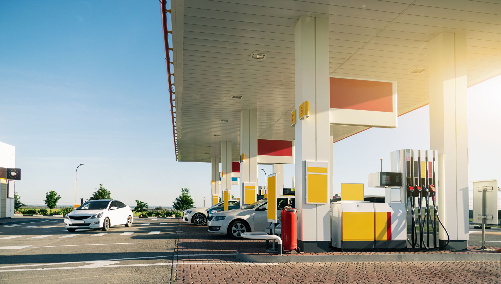 Gas station canopy with fuel pumps and a white car under bright sunlight