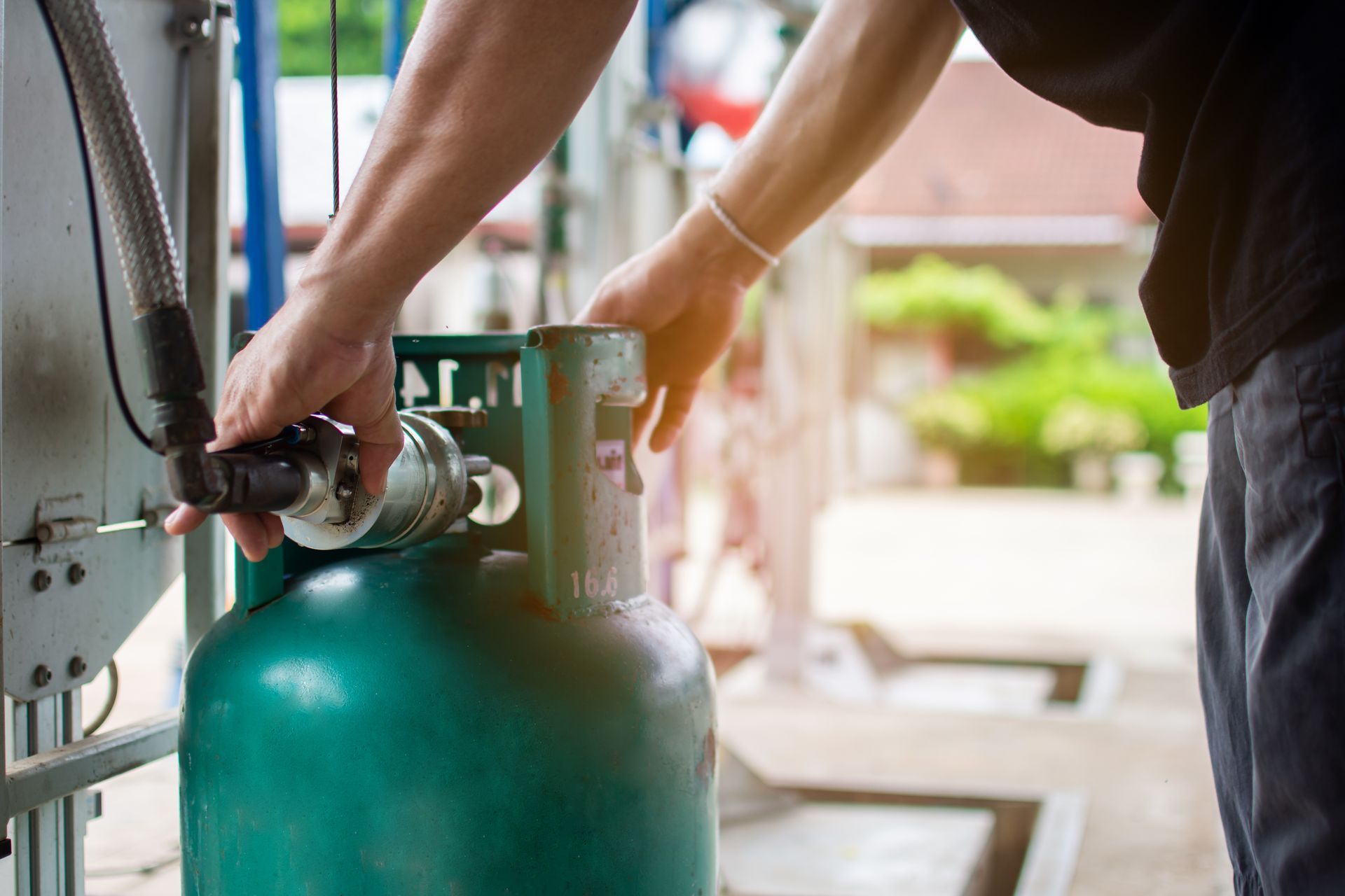 Person connecting a fuel nozzle to a large gas cylinder at a service station.
