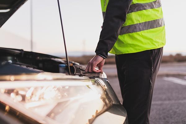 Person in a neon safety vest inspecting a car with its hood open