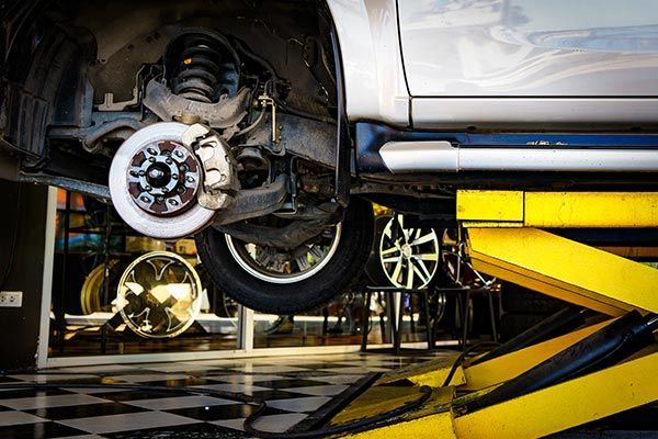 Changing Tire at Auto Repair Shop Garage — Grants Pass, OR — Fairgrounds Towing & Fuel LLC Car lifted on a yellow hydraulic lift, showing wheel and brake assembly in an auto repair shop