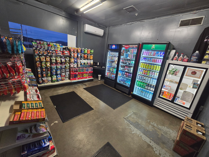 A White Tow Truck — Grants Pass, OR — Fairgrounds Towing & Fuel LLC Small convenience store interior with snack shelves, coolers, and a few floor mats on a gray floor.