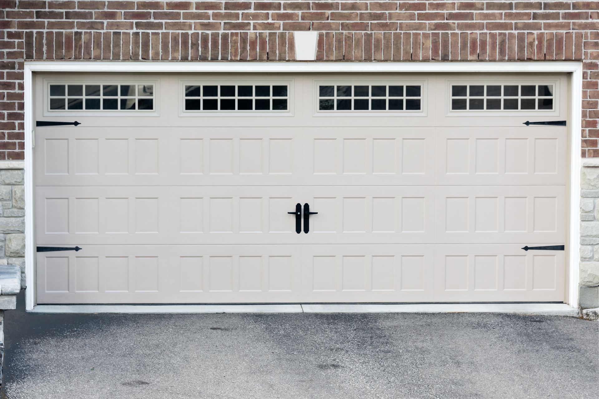 Tan garage door with small windows, black hardware, set in brick and stone.