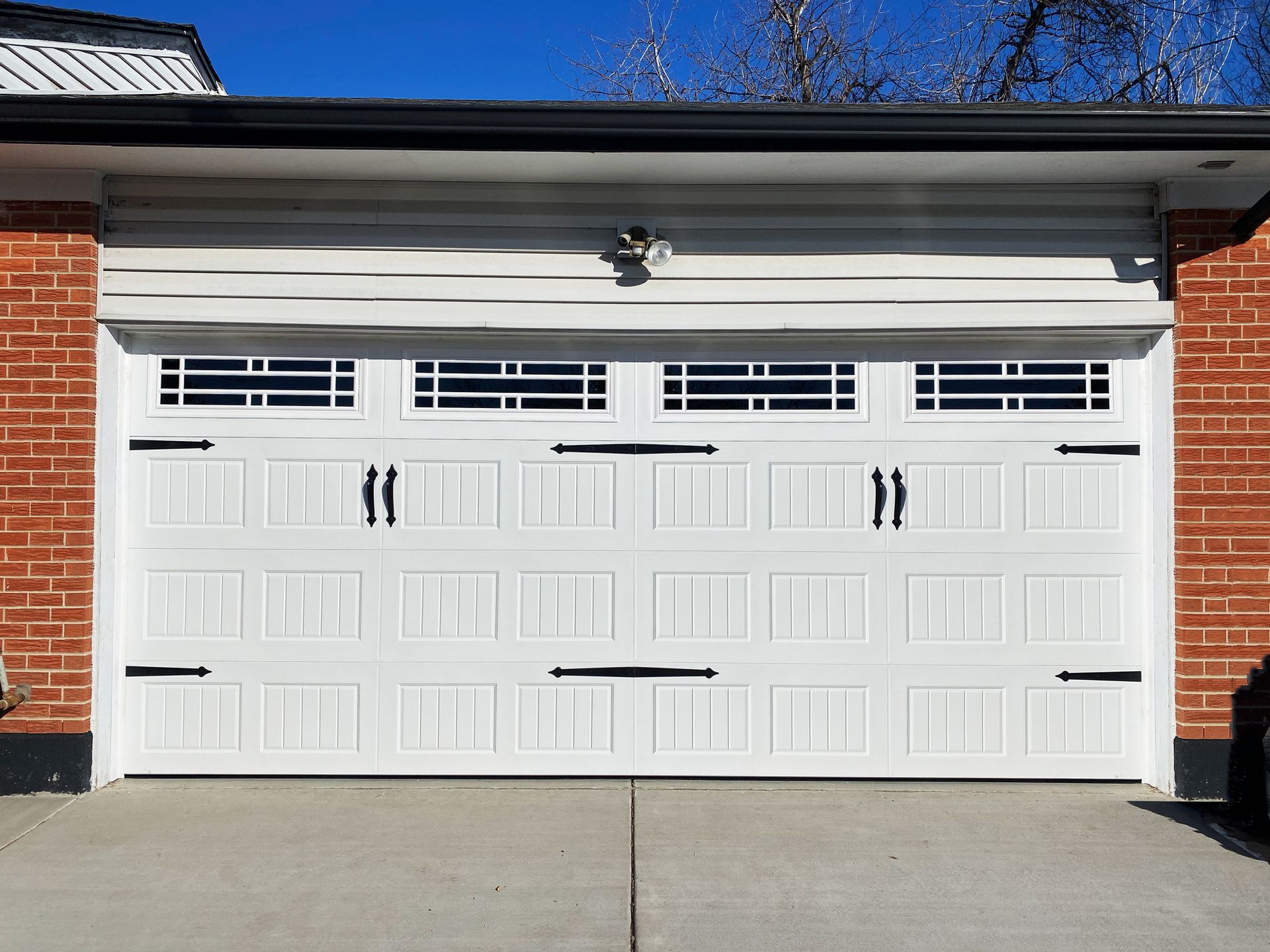 White garage door with decorative hardware and windows; red brick exterior.