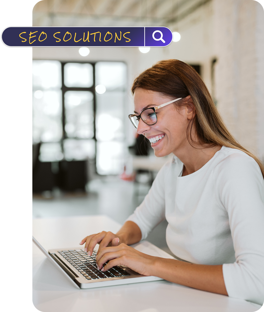 Woman with glasses smiles while typing on a laptop;