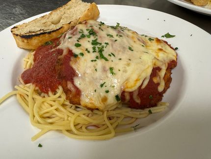 Plate of spaghetti with marinara and melted cheese, topped with parsley and served with toasted bread