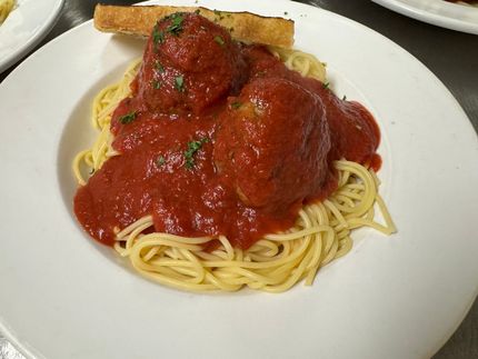 Spaghetti topped with red tomato sauce and meatballs on a white plate