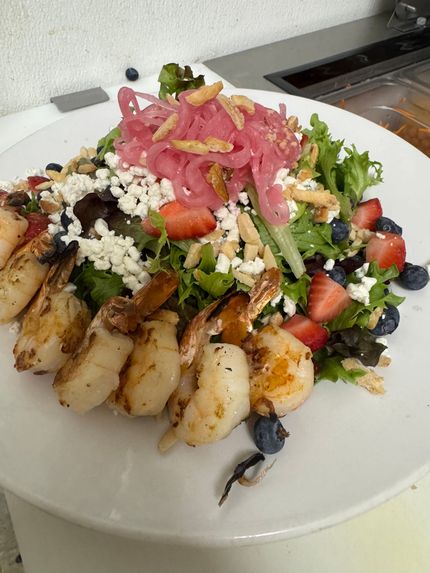 Grilled shrimp and strawberry salad with feta, greens, and pickled red onions on a white plate