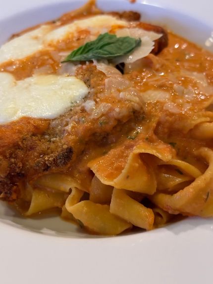 Pasta with meat sauce, melted cheese, and basil on a white plate