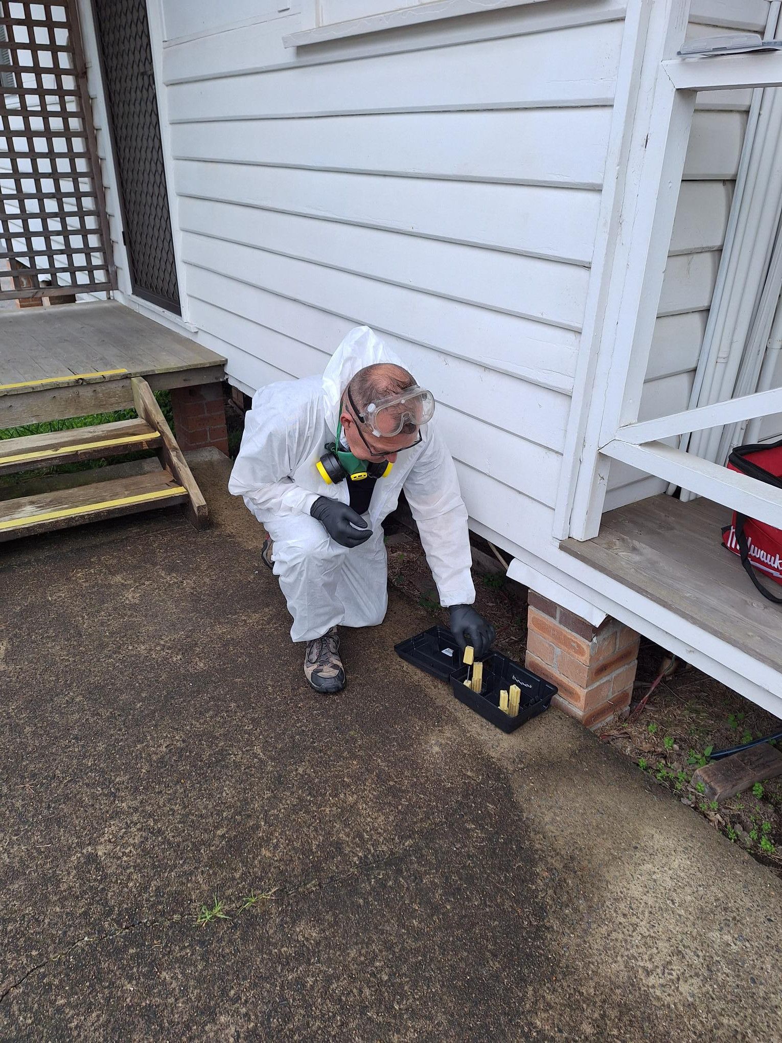 Person in protective suit inspecting a termite bait station near a white house. — Bug Crazy Pest Control in Port Macquarie, NSW
