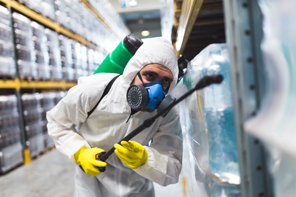 A Man in a Protective Suit and Mask is Spraying Chemicals in a Warehouse — Bug Crazy Pest Control in Port Macquarie, NSW