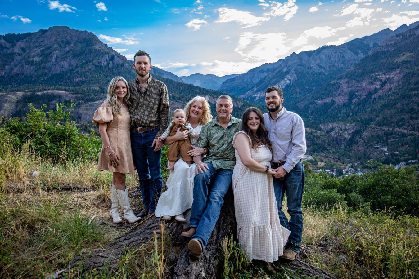 Family group posing on a mountain overlook with forested valley and blue sky at sunset