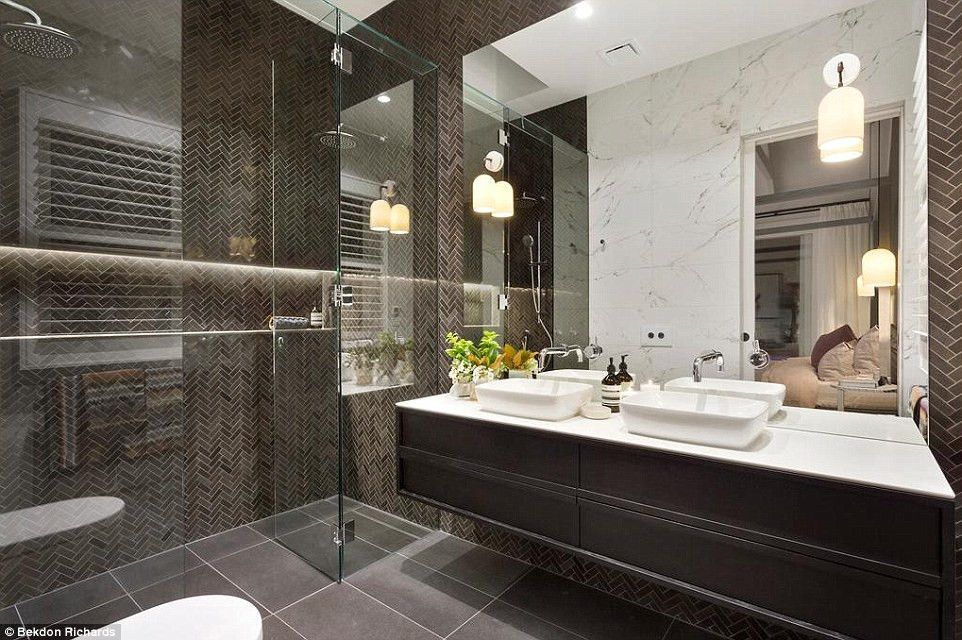 Modern bathroom with dark brown tiles, double sink, glass shower, and hanging lights.