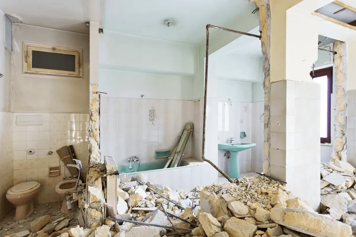 A Man Is Kneeling Down In A Bathroom Holding A Hammer — Ultimate Bathrooms Ballarat In Alfredton, VIC