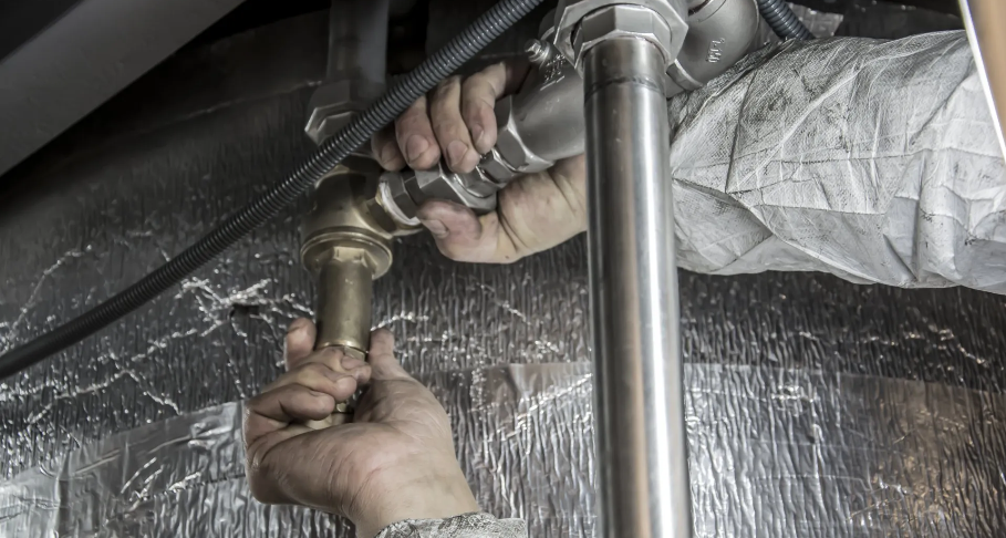 Hands connect plumbing pipes in a basement.
