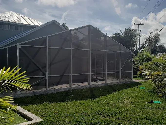 Screened-in patio extension attached to a house with green lawn and landscaping.