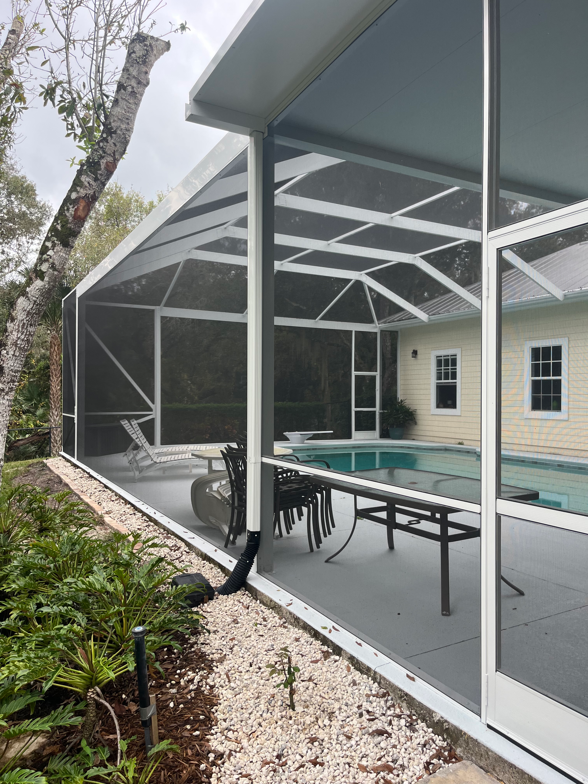 Screened-in pool enclosure with white frame, clear windows, and dark mesh panels. Contains pool and patio furniture.