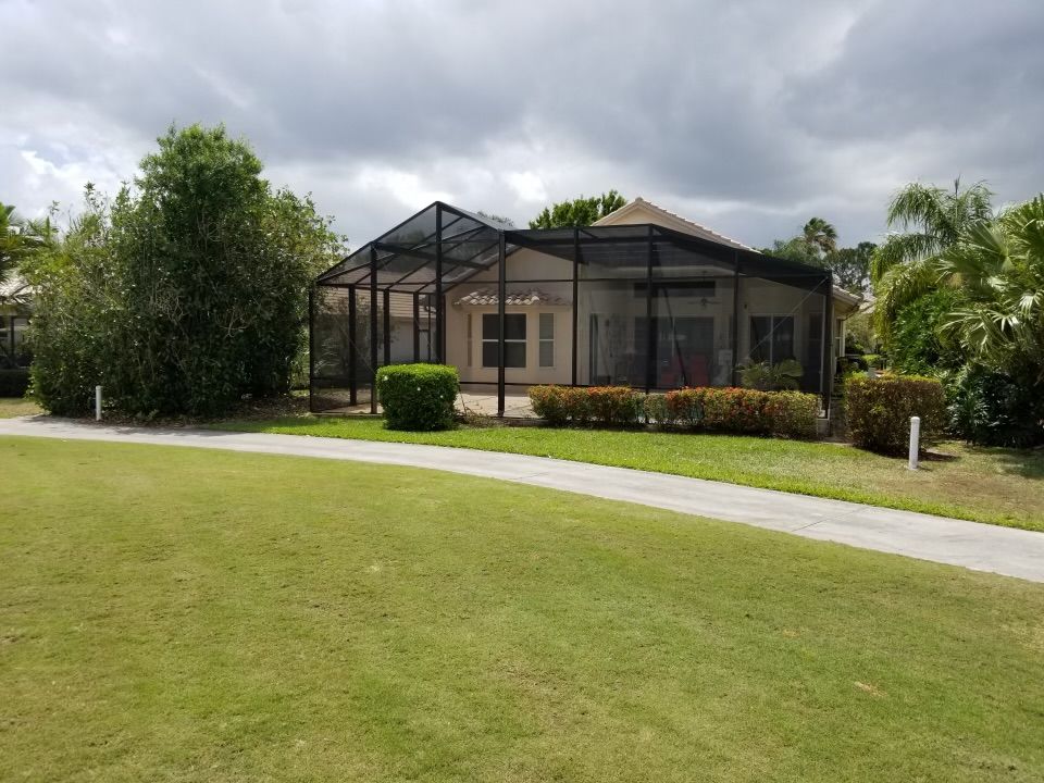 Black-screened structure, likely a patio or pool enclosure, on a grassy area, path in front, under a cloudy sky.