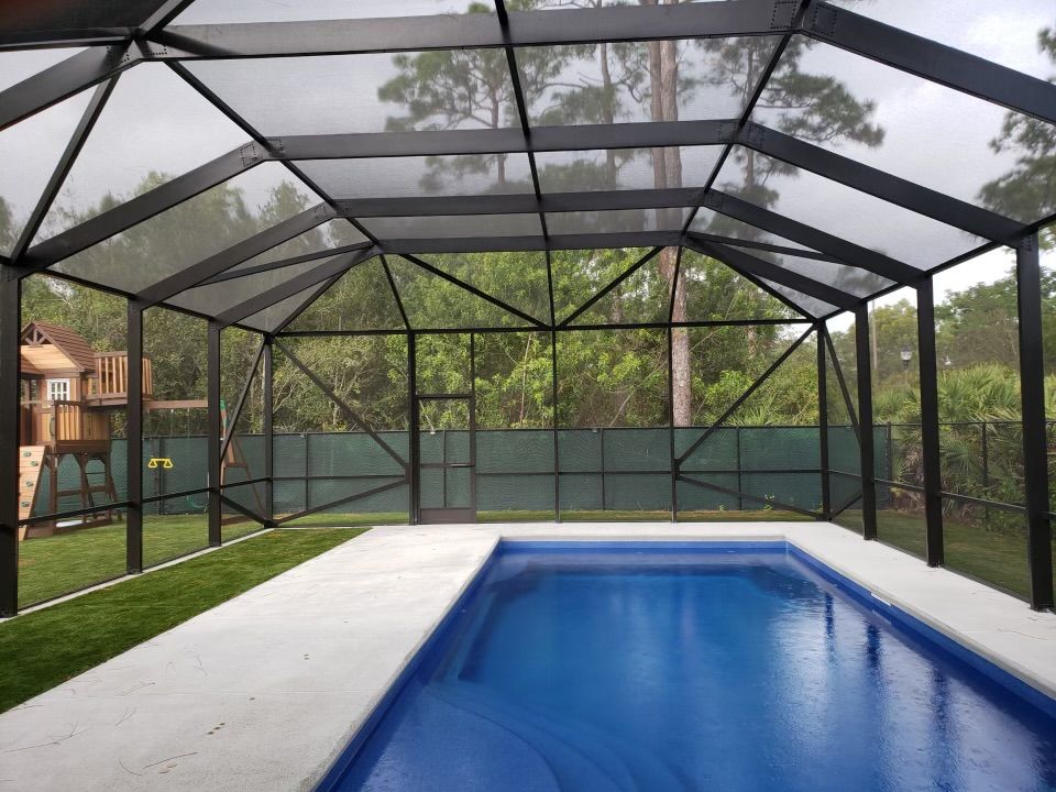 Pool enclosed by a black screened structure, with blue water and surrounding greenery.