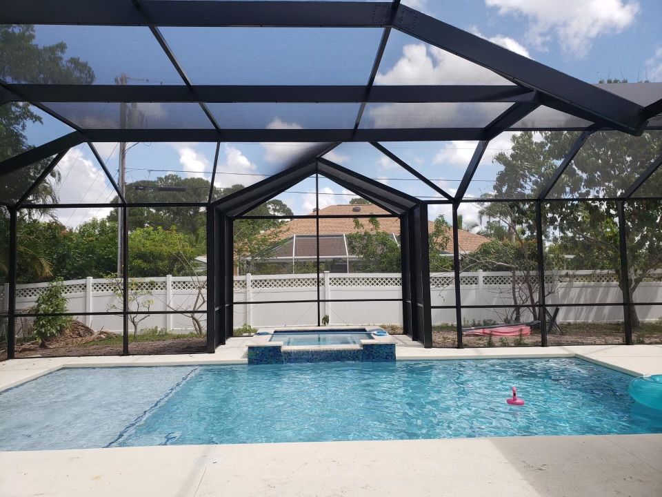 Pool enclosed by a black screened structure under a partly cloudy sky.
