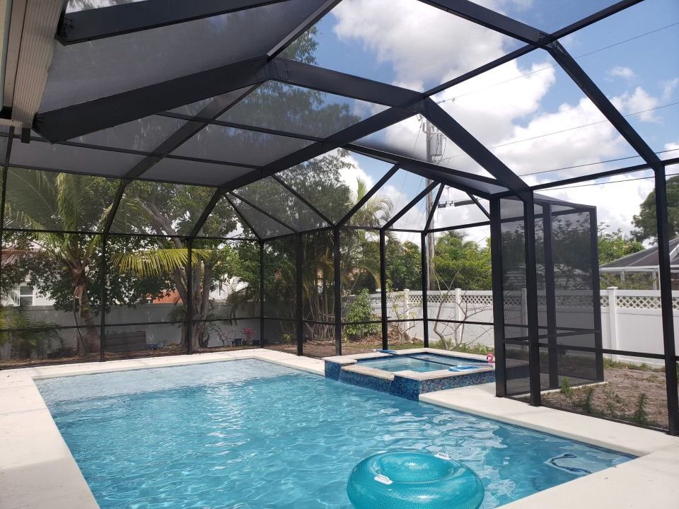 Pool enclosed by a black screen structure under a bright sky. Blue pool, a hot tub, and an inflatable.