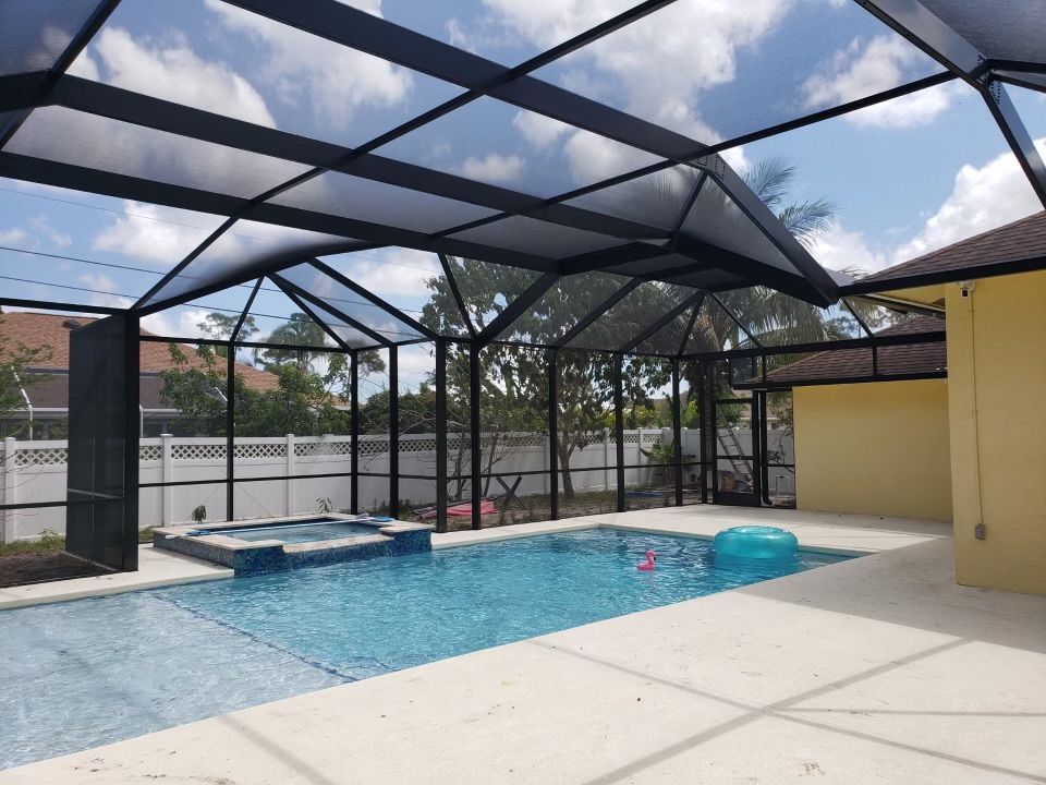Pool area with screened enclosure. Pool, hot tub, and patio under a black frame roof.