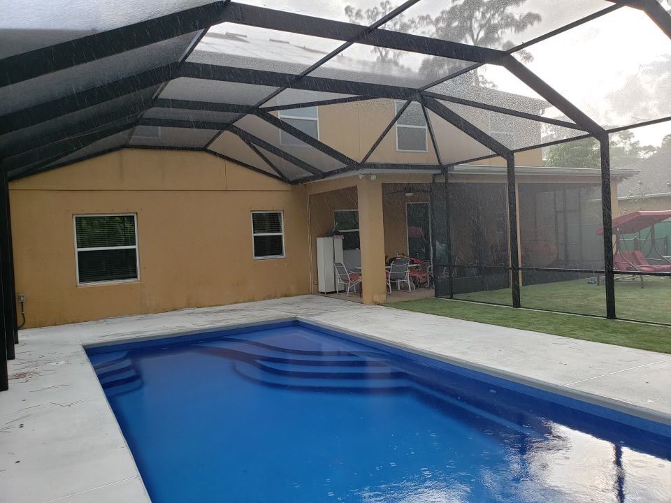 Pool with screen enclosure, house in background, overcast day.