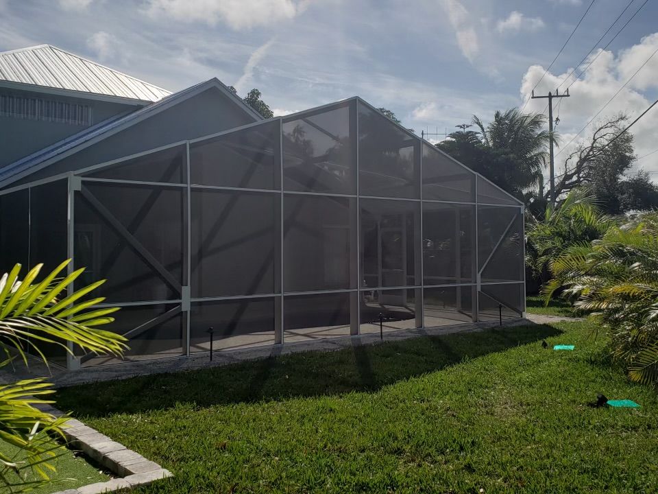 Screened-in patio with a green lawn in front of a house, under a sunny sky.
