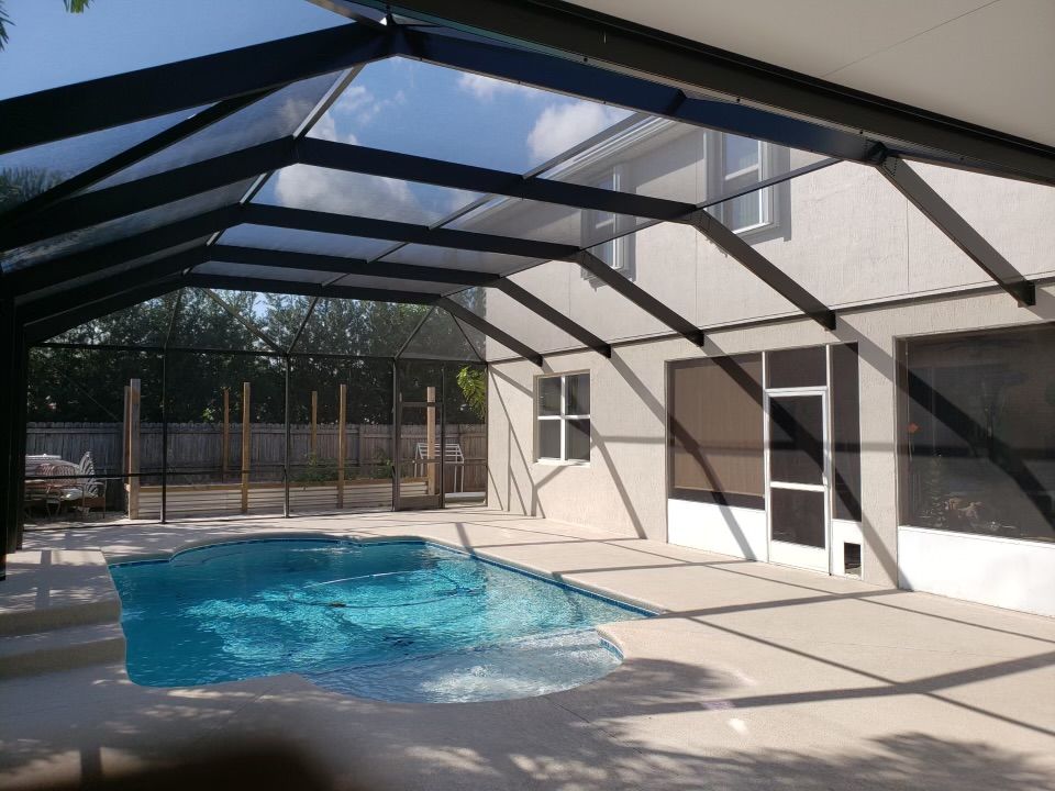 Pool area with screened enclosure, pool, patio, and house. Blue water, sunlight, black framing.