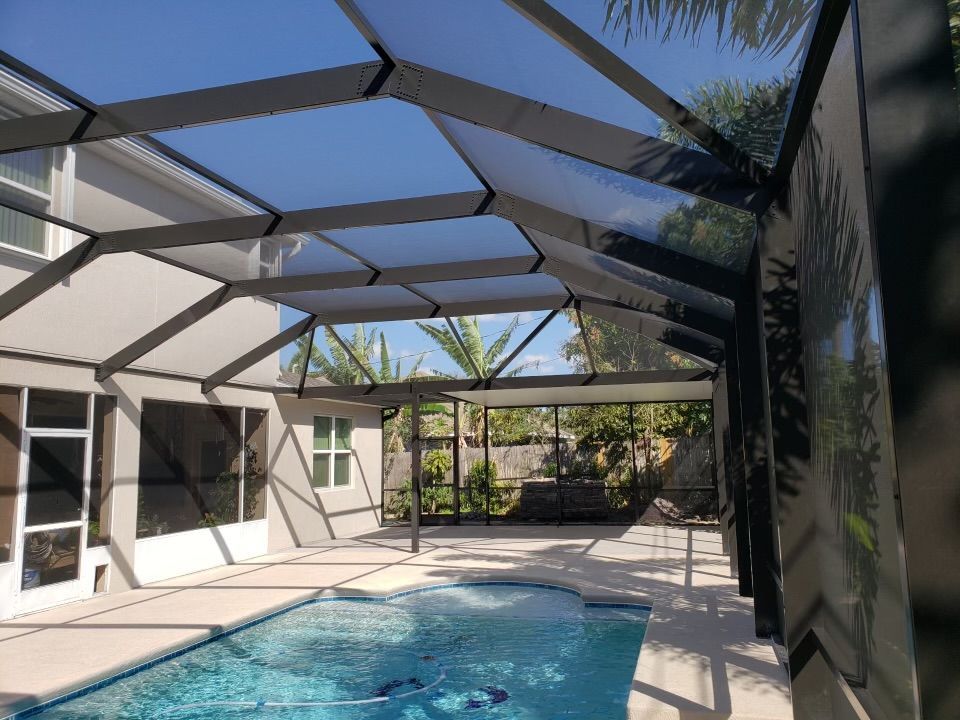 Pool area enclosed by a screen structure with geometric roof panels and a pool of water.