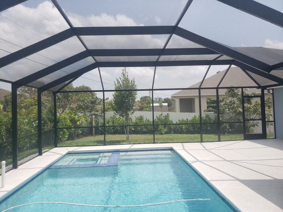 Swimming pool enclosed by black-framed screen with a concrete patio.