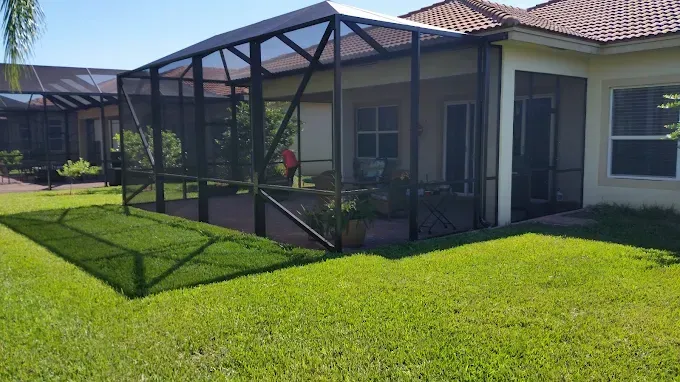 Black screened patio extension attached to a beige house, over green grass.
